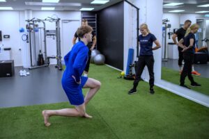 urheilija tekee askelkyykkyä, fysioterapeutti seisoo edessä ja tarkkailee tekemistä